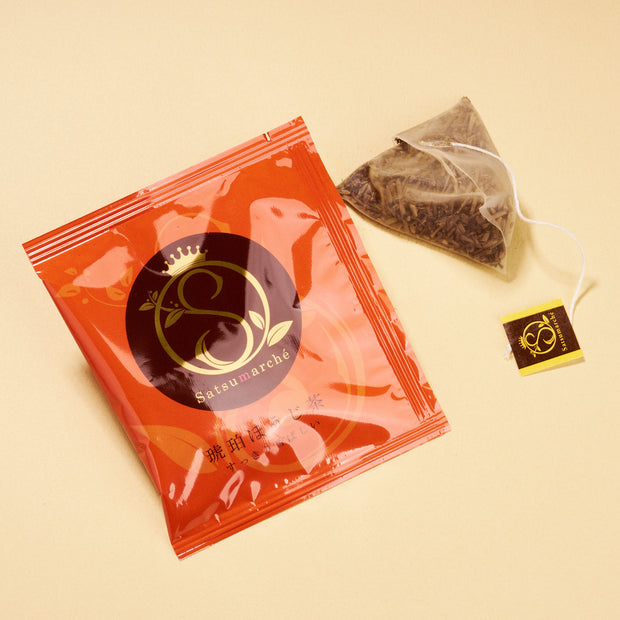 A red tea packet from April '26 Bokksu: Handpicked in Japan rests beside a pyramid tea bag with a matching tag on a light beige surface, highlighting this regional Japanese specialty.