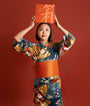 A woman in a floral kimono holds the Bokksu Snack Box: Seasons of Japan above her head against an orange background, inviting you to discover the authentic flavors of Japan. thumbnail 24