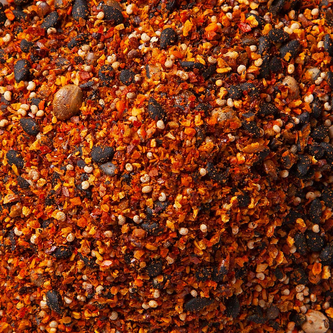 Close-up of S&B Shichimi Togarashi Seven-Spice Pepper, a blend from Japanese cuisine featuring a textured mix of red, orange, and dark brown granules and seeds.