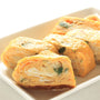 Four pieces of rolled omelette with visible green herbs are arranged on a rectangular white plate, their rich umami flavor elevated by the subtle addition of Bokksu Tinned Shirasu Anchovies with Black Pepper and Basil-Infused Oil. thumbnail 3