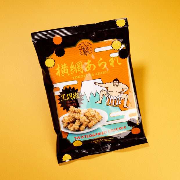 A bag from April '26 Bokksu: Handpicked in Japan features twisted and fried black pepper Yokozuna Arare crackers, with a sumo wrestler design on the front and displayed on a yellow background.