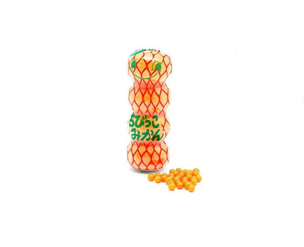 A small plastic bottle adorned with a netted orange design and Japanese text sits beside a pile of tiny orange candy balls on a white background—just one example of the delightful treats you’ll find in the Dagashi Snack Crate 30-Piece Japanese Snack Variety Box, featuring candy, chocolate, cookies, mochi, and Ramune for fans of unique Japanese snacks.